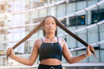 Black teenage girl with afro braided hair, taking her braids with serious expression. With a office...
