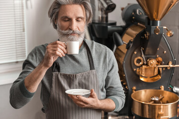 Senior man with cup of hot beverage near modern coffee roaster
