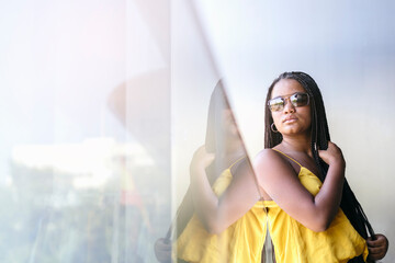 Black teenage girl with afro braided hair and sunglasses, looking away with serious expression....