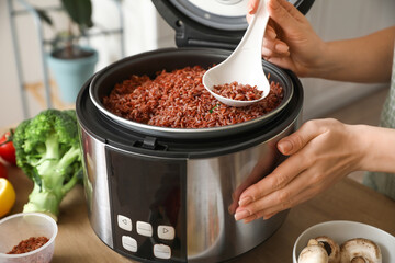 Woman preparing rice in multi cooker at  kitchen table
