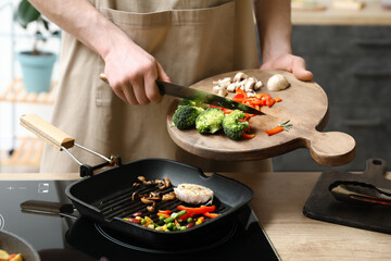 Man frying tasty vegetables in kitchen
