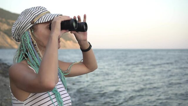 Young attractive woman looks through binoculars towards the sea
