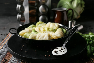 Frying pan with uncooked cabbage rolls on dark background