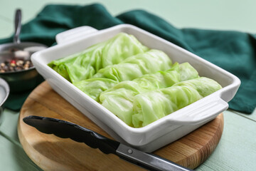 Baking dish with uncooked cabbage rolls on color wooden background