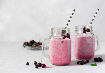 Obraz na płótnie Canvas Smoothie with natural yogurt and black currant with drinking straw in glass jars on light gray background. Copy space