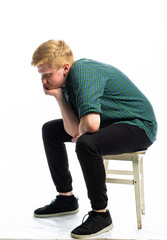 portrait of a red-haired guy in a green shirt and jeans on a white isolated background. teenager sitting on an old stool