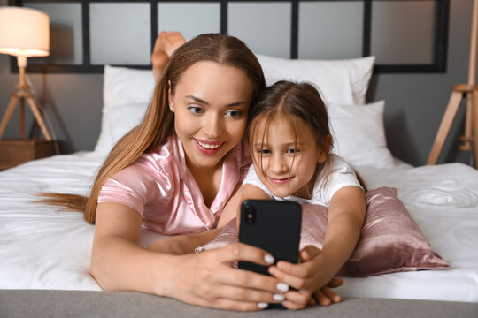 Young woman and her little daughter taking selfie in bedroom