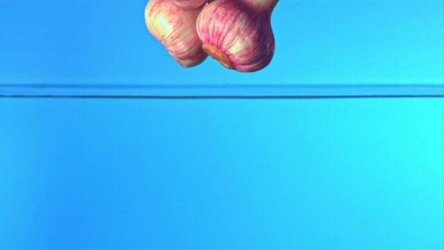 Super slow motion fresh garlic falls into the water with splashes on a blue background. Filmed on a high-speed camera at 1000 fps. High quality FullHD footage