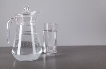 Glass and jug with of water, on  gray background.