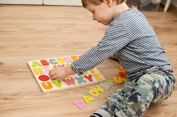 Two year boy playing with wooden alphabet letters board on the floor. Intellectual game, preschool...