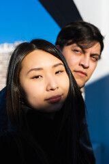 vertical photo of asian american woman with her interracial partner, latino man sky background,...