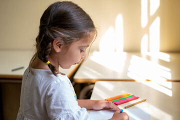 Adorable niña en su primer día de colegio  vestida con mandilón a cuadros verdes dibujando y mirando libros.