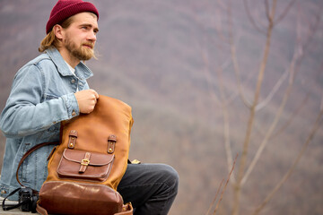 tourist man tourist man opening leather brown backpack during hike in mountains, sit having rest,...
