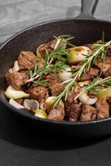 Diced Aberdeen Angus beef with shallots and rosemary, fried in a cast iron frying pan.  Selective colour image