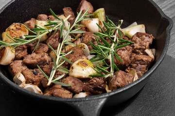Diced Aberdeen Angus beef with shallots and rosemary, fried in a cast iron frying pan.  Selective colour image