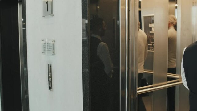Medium shot of young male bellboy escorting mature businessman to his hotel room, carrying his suitcase as going up in elevator together