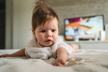Fototapeta premium Front view of small healthy caucasian baby three months old boy or girl lying on the bed at home with belly down in bright room with copy space