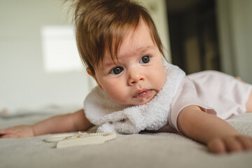 Small caucasian baby four months old lying on the bed at home in bright room in day with copy space looking to the side belly down
