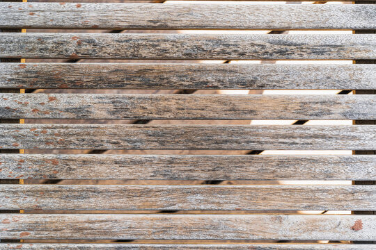 Slatted deck of an old beach lounger. Close-up. The structure of a tree that has aged from time and weather is visible. A floor of planks is visible in the gap. Background. Texture.