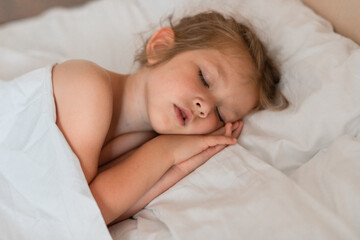 Fototapeta na wymiar Adorable little girl sleeping in bed with white linens. Place for your text. Healthy baby sleep.