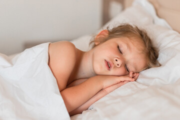 Adorable little girl sleeping in bed with white linens. Place for your text. Healthy baby sleep.