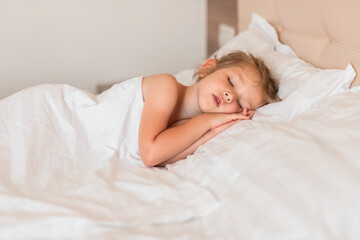 Adorable little girl sleeping in bed with white linens. Place for your text. Healthy baby sleep.