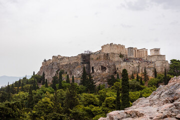 Fototapeta na wymiar Acropolis hill (Parthenon, Propylaea, Temple of Athena Nike, Hekatompedon Temple) in greenery, Athens ancient historical landmark in city center with rocky Areopagus - Hill on cloudy day