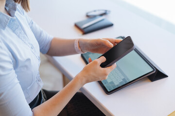 Female hands holding a smartphone with black screen on working background, papers, tablet , white desk