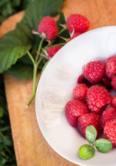 A plate with fresh raspberries on a wooden cutting board, next to a fresh berry, green leaves on the grass. The concept of a diet, eco-food, separate nutrition, veganism, a healthy lifestyle.
