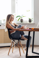 CAucasian freelancer woman work from home. Female hold tea chatting or watching movie use laptop. Modern girl relaxing at kitchen surfing internet