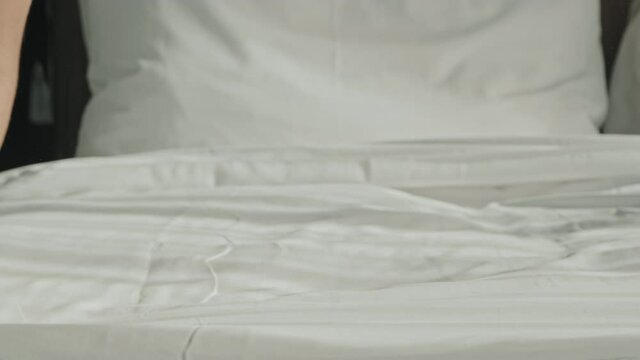Slowmo close-up of unrecognizable female housekeeper making bed in hotel room with clean white linens