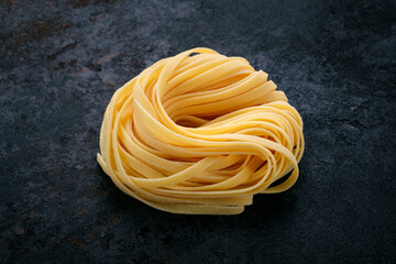 Fresh raw tagliolini pasta rolled with a nest on a stone background. Type of Italian pasta