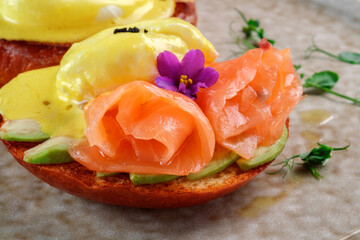 Breakfast with salmon, egg benedict and avocado on a toasted bun. Healthy breakfast in the morning on the table