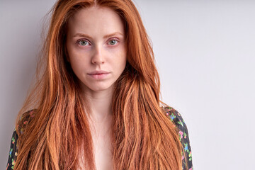Close-up portrait of redhead young female in black dress looking at camera confidently, isolated on white studio background. Serious female with natural long red hair having no make-up. copy space.