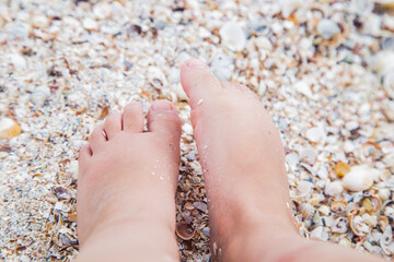 Children's feet are standing on the beach on the yellow sunny sand.