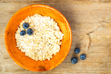 Oatmeal porridge and blueberry in orange bamboo bowl on wooden table background. Healthy breakfast concept. Top view. Flat lay. Close up. Selective soft focus. Shallow depth of field. Text copy space.