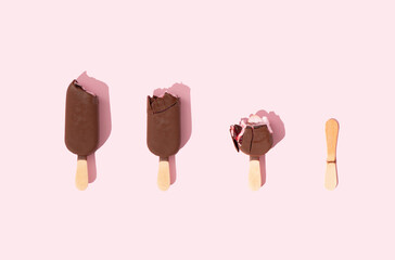 Ice cream on stick in the process of eating on pastel pink background. Refreshment frozen food pattern concept. Sorted by size. Top view. Flat lay