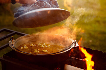 A woman cook opens the lid of a saucepan or cauldron in which pilaf.