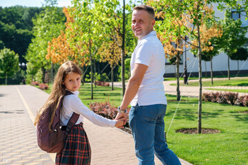 Fototapeta premium Daughter in school uniform and father walking together to school down the street, holding hands, back view