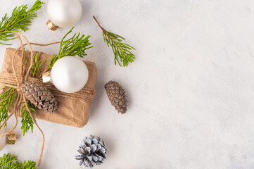 Stylish Christmas composition on a plain white background. Coniferous branches, gift, cones and white Christmas balls. Minimalism. Low angle view. New Year, Christmas, Christmastide.