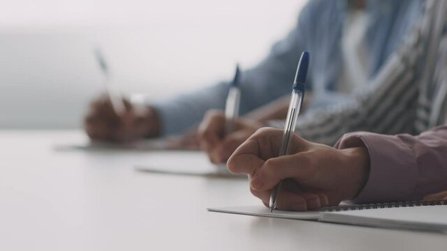 Group of unrecognizable diverse university students writing in copybooks, noting lecture, close up, slow motion