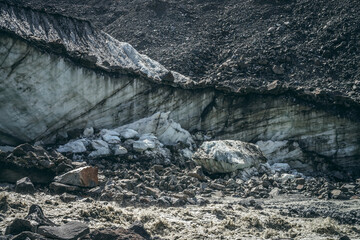 Scenic landscape with powerful mountain river beginning from glacier with ice chunks. Beautiful scenery with glacier at source of turbulent glacial river. Mountain river among moraines and ice blocks.