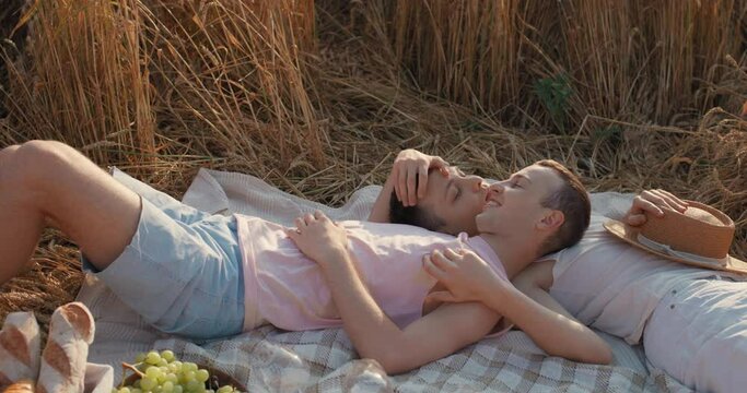 Cheerful Couple Guys Lovers Resting in the Field stroking Each Other with Love. Two Handsome Men lying on a Picnic Blanket Having a Date. Enjoys Time Together. Summer Vacation. Cute LGBT relationship.