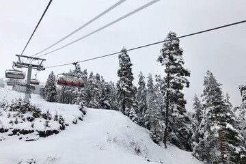 Fototapeta na wymiar Outdoor four-seater lift rises above the ski slope in high white winter mountains, ski season, winter activities