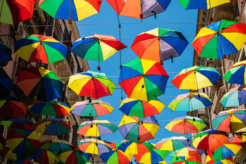 Fototapeta na wymiar Colorful umbrellas background. Rainbow colors umbrellas in the sky hanging out above the old streets of Catania, Sicily. Street decoration.