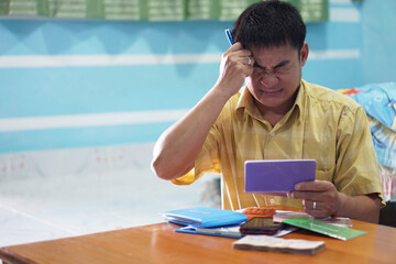 Middle-aged Asian man is looking at bank book and feels headache. Concept : Life planning....