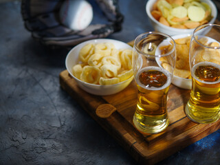 Beer in glasses, chips, onion rings, snacks. A baseball glove and a ball are nearby. Relaxing with friends, watching a baseball game. Hobby, rest, relaxation. High angle view.
