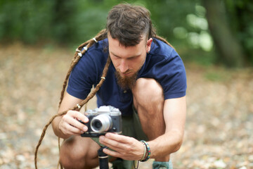 Young artist with dreadlocks setting up his digital camera on a gimbal, a handheld stabilizer, getting ready to shoot some footage in a forest