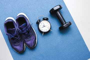 A pair of  running shoes with alarm clock and barbell on a blue mat for sport background
