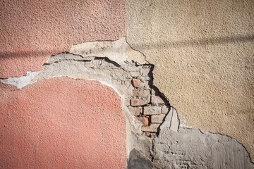 Plaster peeling from a facade wall on a residential building, with a hole letting the brick visible on a decayed home needing renovation...